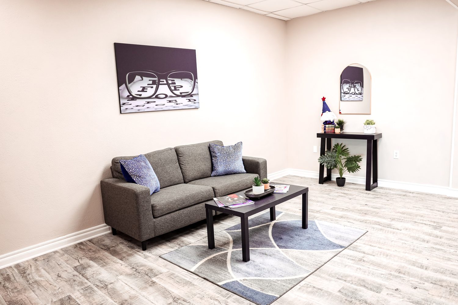 Quiet sitting area at Eye Koni Optical — gray sofa, eye-chart artwork on the wall, and a console with plants
