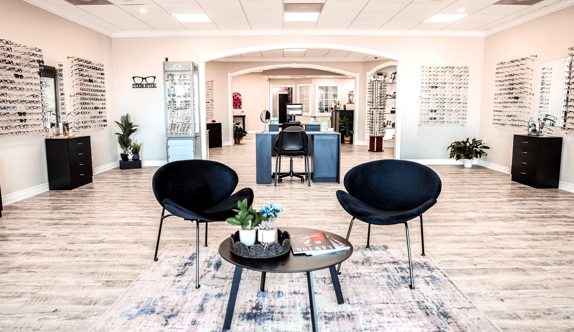 The showroom at Eye Koni Optical — symmetrical view through the arched entry with navy lounge chairs, frame walls on both sides, and the Oakley case